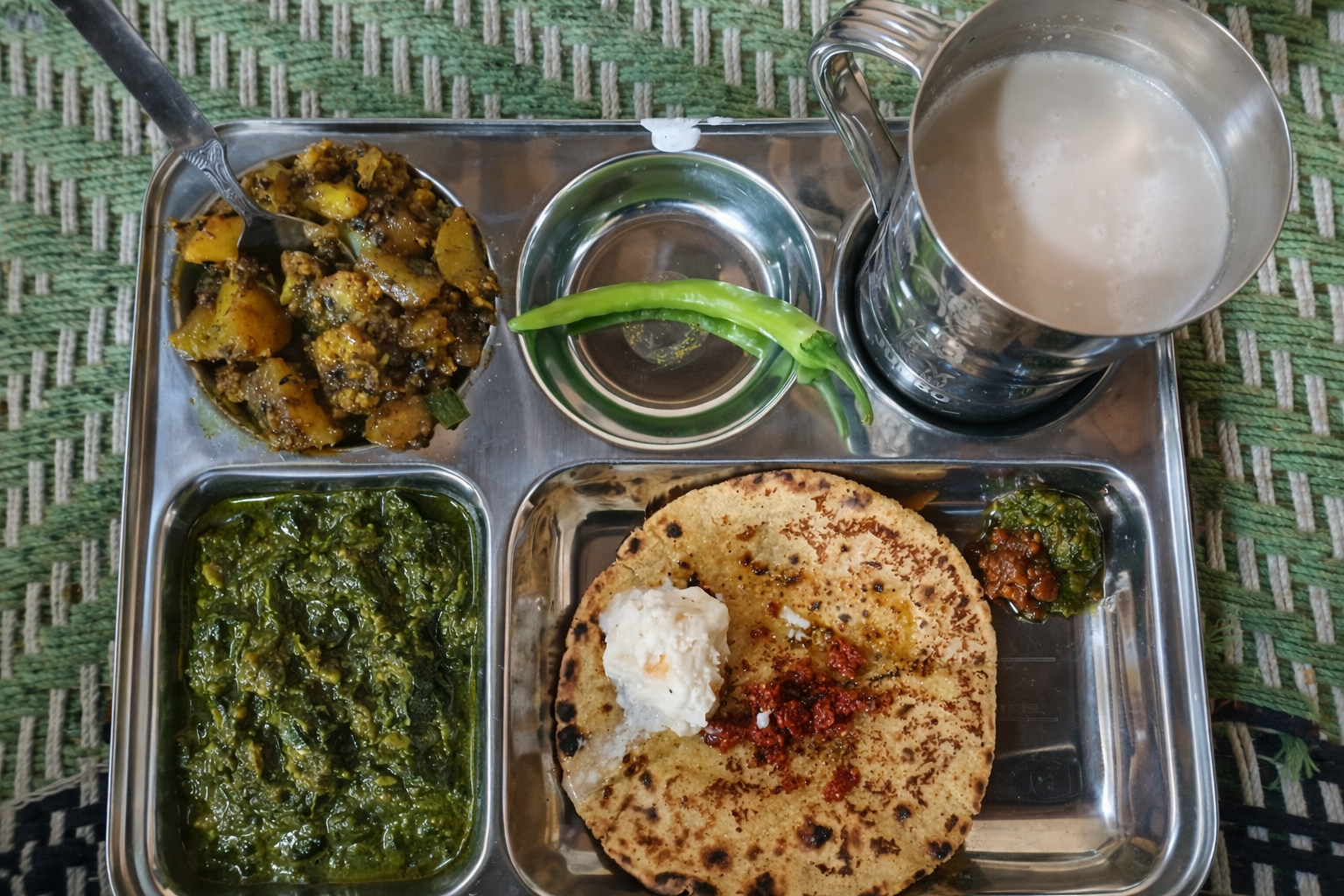 Traditional steel thali with roti, saag, and lassi